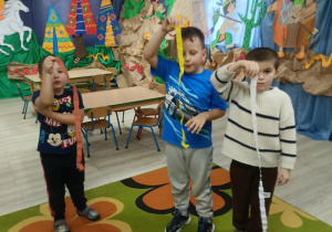 Chłopcy wykonują ćwiczenia oddechowe z pomocą bibuły.