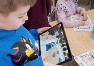 Mikołaj trzyma tablet na którym znajdują się bohaterowie z jego kolorowanki.