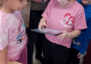 Emma trzyma tablet na którym znajdują się bohaterowie z jej kolorowanki.