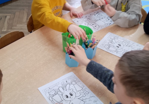 Grupka dzieci siedzi przy stoliku i koloruje obrazki.
