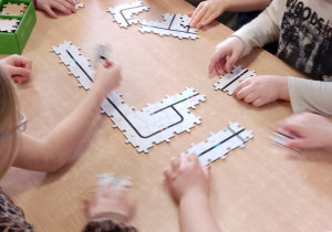 Grupka dzieci siedzi przy stoliku i układają z elementów trasę do Ozobotów.