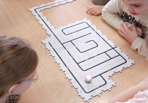 Grupa dzieci obserwuje, jak Ozobot pokonuje trasę.