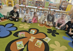 Dzieci siedzą na dywanie. Przed nimi leża książki z serii "Przygody Franklina" oraz obrazek z wizerunkiem Małego Misia.