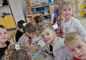 Przedszkolaki siedząc przy stoliku tworzą plakat.