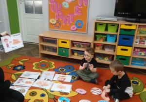 Filip i Franek patrzą na ilustracje pączków, którą pokazuje logopeda.