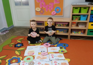 Filip i Franek trzymają w dłoniach ilustracje pączków.