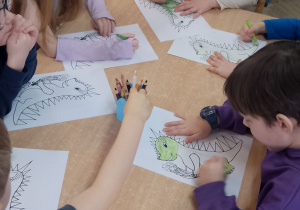Dzieci siedzą przy stole i kolorują postać Dinka - maskotki Programu przedszkolnej edukacji antytytoniowej "Czyste powietrze wokół nas".