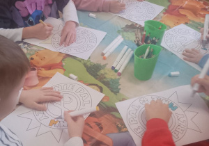 Grupka dzieci siedzi przy stole i koloruje znaki "Nie pal przy mnie".