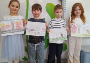 Czworo dzieci stoi obok siebie i prezentuje wykonane przez siebie obrazki do opowiadania "O kominie, który przestał dymić".
