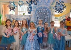 Zdjęcie grupowe dziewczynek w strojach Elzy na tle dekoracji z otrzymanymi upominkami.