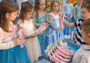 Antek i Mikołaj wręczają dziewczynkom torebki z motywem Elzy. W tle dekoracja.