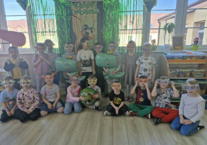 Dzieci w dinozaurowych okularach pozują do zdjęcia na tle dekoracji w sali.