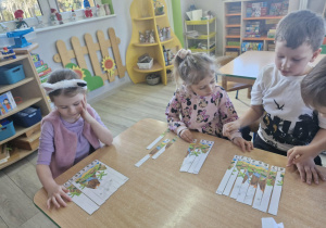 Ola, Liliana i Franek układają pocięte na części obrazki z dinozaurami.