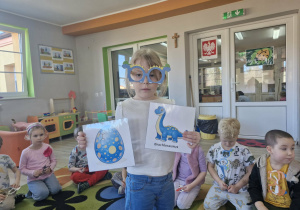 Nadia trzyma w dłoniach obrazki z dinozaurem i jajem dinozaura.