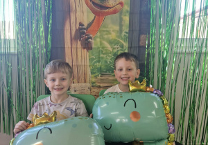 Olek i Franek pozują do zdjęcia przy dinozaurowej ściance.