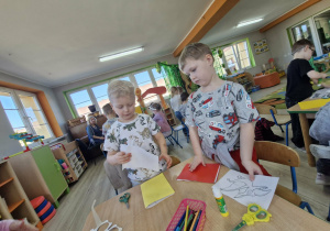 Karol i Wojtuś przy stolikach projektują swoje książki o dinozaurach.