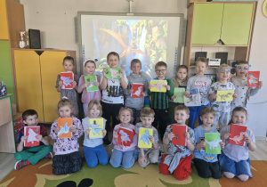 Dzieci stoją przed tablicą i prezentują wykonane przez siebie książki o dinozaurach.