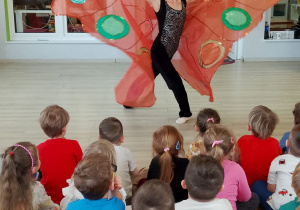 Przedszkolaki siedzą na dywanie, a przed nimi tancerka w pięknym stroju prezentuje "Taniec motyla".