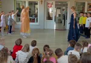 Po lewej stronie stoi sześć dziewczynek, a po prawej sześciu chłopców. Dzieci naśladują ruchy baletnic.