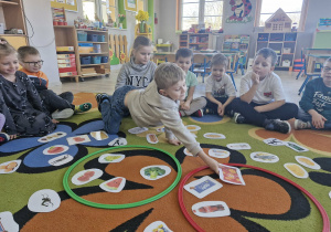 Na dywanie leżą dwa okręgi i obrazki z produktami spożywczymi. Dzieci dzielą je na zdrowe i niezdrowe.