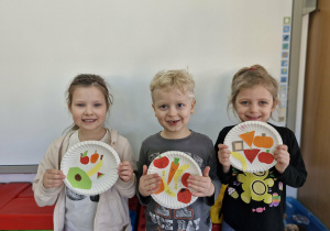 Maja Karol i Liliana prezentują wykonane przez siebie prace plastyczne: talerze pełne zdrowej żywności.
