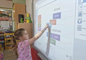 Weronika stoi przy tablicy multimedialnej i rozwiązuje quiz dotyczący zdrowego żywienia.