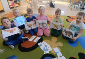 1. Dzieci trzymają w rękach ilustracje przedstawiające dinozaury.