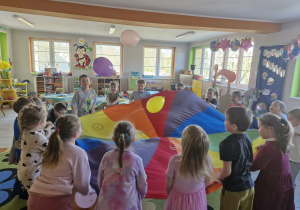 Dzieci w trakcie zabawy z chustą animacyjną, na której podrzucają kolorowe balony.