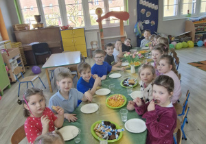 Przedszkolaki siedzą przy nakrytym stole w trakcie słodkiego poczęstunku.
