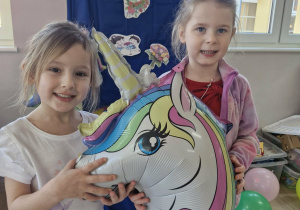 Zuzia i Ola pozują do zdjęcia z balonem w kształcie jednorożca.