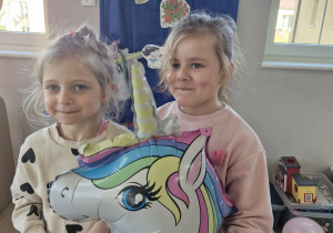 Liliana i Weronika pozują trzymając w dłoniach balon z jednorożcem.