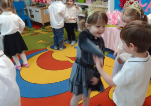 Dzieci tańczą w parach przy muzyce, dziewczynki na głowach mają złote diademy.