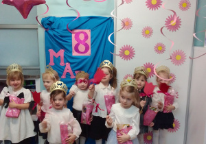 Dziewczynki z upominkami w dłoniach pozują do zdjęcia na tle dekoracji z okazji 8 marca.