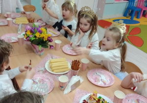 Dzieci przy stole, na którym są słodycze i wiosenne dekoracja.