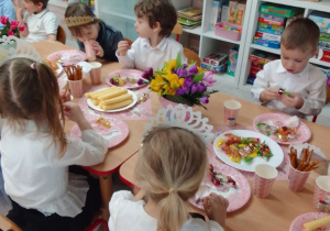 Dzieci siedzą przy stole, na którym są słodycze i wiosenne dekoracja.