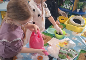 Zuzia podlewa rzeżuchę konewką. Obok stoją koleżanki.