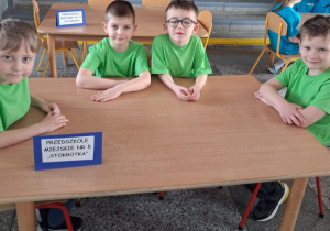 Czterech chłopców w zielonych koszulkach siedzi przy stoliku.