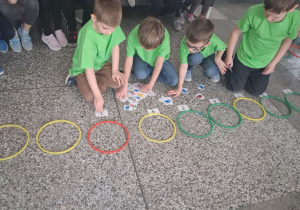 Chłopcy siedzą na podłodze i w kolorowych obręczach dopasowują elementy zbiorów w określonej liczbie.