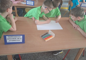 Mikołaj rysuje kredkami obrazek według wskazówek prowadzącej. Obok siedzą chłopcy.