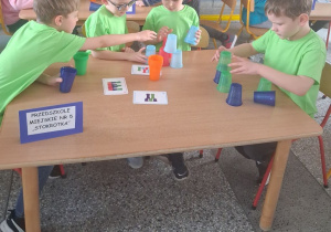 Chłopcy przy stoliku układają kolorowe kubeczki według wzoru.