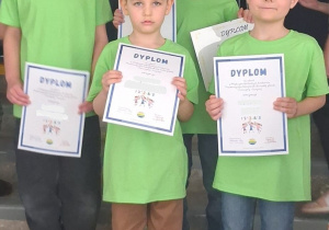 Grupa "Słoneczek" pozuje do zdjęcia na schodach w budynku szkoły prezentując otrzymane dyplomy.