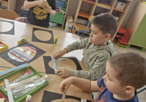 Dzieci siedzą przy stoliku w trakcie tworzenia pracy plastycznej.