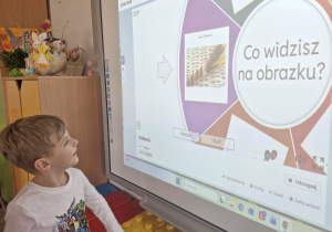 Olek stoi przed tablicą multimedialną, na której widać palmę wielkanocną.