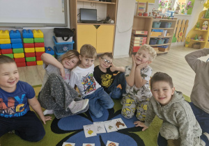 Dzieci siedzą na dywanie; przed nimi leżą obrazki przedstawiające pisanki i kurczaczki.