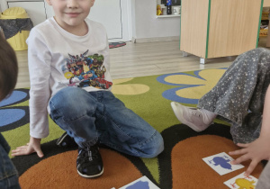 Oluś siedzi na dywanie; przed chłopcem leża kartoniki z wielkanocnymi obrazkami i pasującymi do nich cieniami.