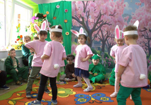 Na scenie tańczą 3-latki w przebraniu zajączków. Mają na sobie różowe koszulki z przyczepionym białym ogonkiem, a na głowach mają opaski.