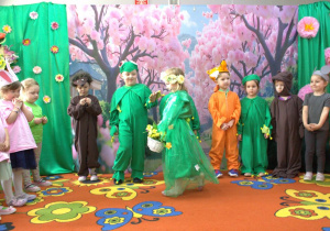 Ala przebrana za Panią Wiosnę chodzi po scenie i trzyma koszyczek z kwiatami.