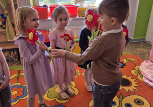 Krzyś wręcza pluszowego kwiatka Ali, obok niej stoi Felicja, która już dostała kwiatka.