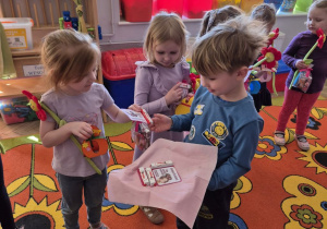 Józio stoi przed Jagodą trzymając w ręku tacę, na której znajdują się wydrukowane karty z batonikiem Kinder. Józio wręcza kartę koleżance.