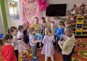 Dziewczynki stoją naprzeciwko chłopców, Jagoda trzyma tackę ze słodkościami dla chłopców. Teraz dziewczynki obdarowują swoich kolegów z grupy słodkościami.